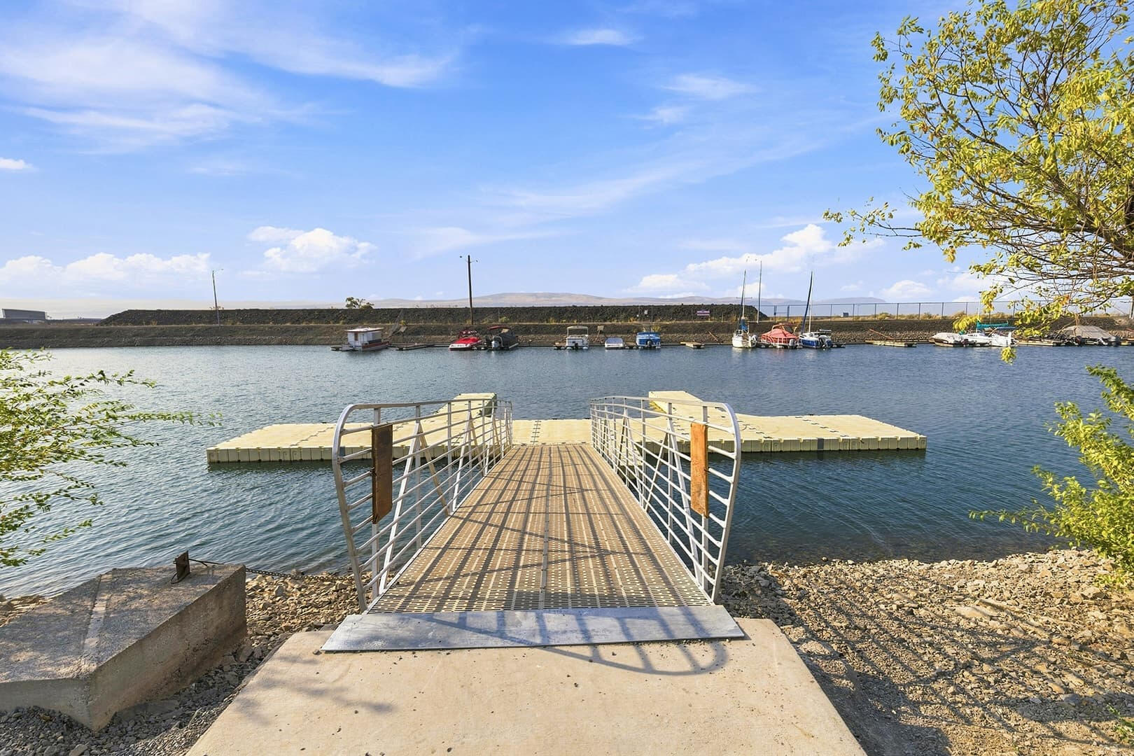Gangway leading to a floating dock on the lake, with leafy branches and shoreline to the side.
