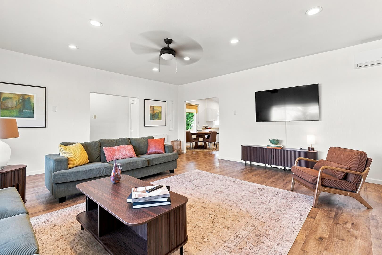 Living room with green seating, a wooden coffee table, patterned rug and wall-mounted television.
