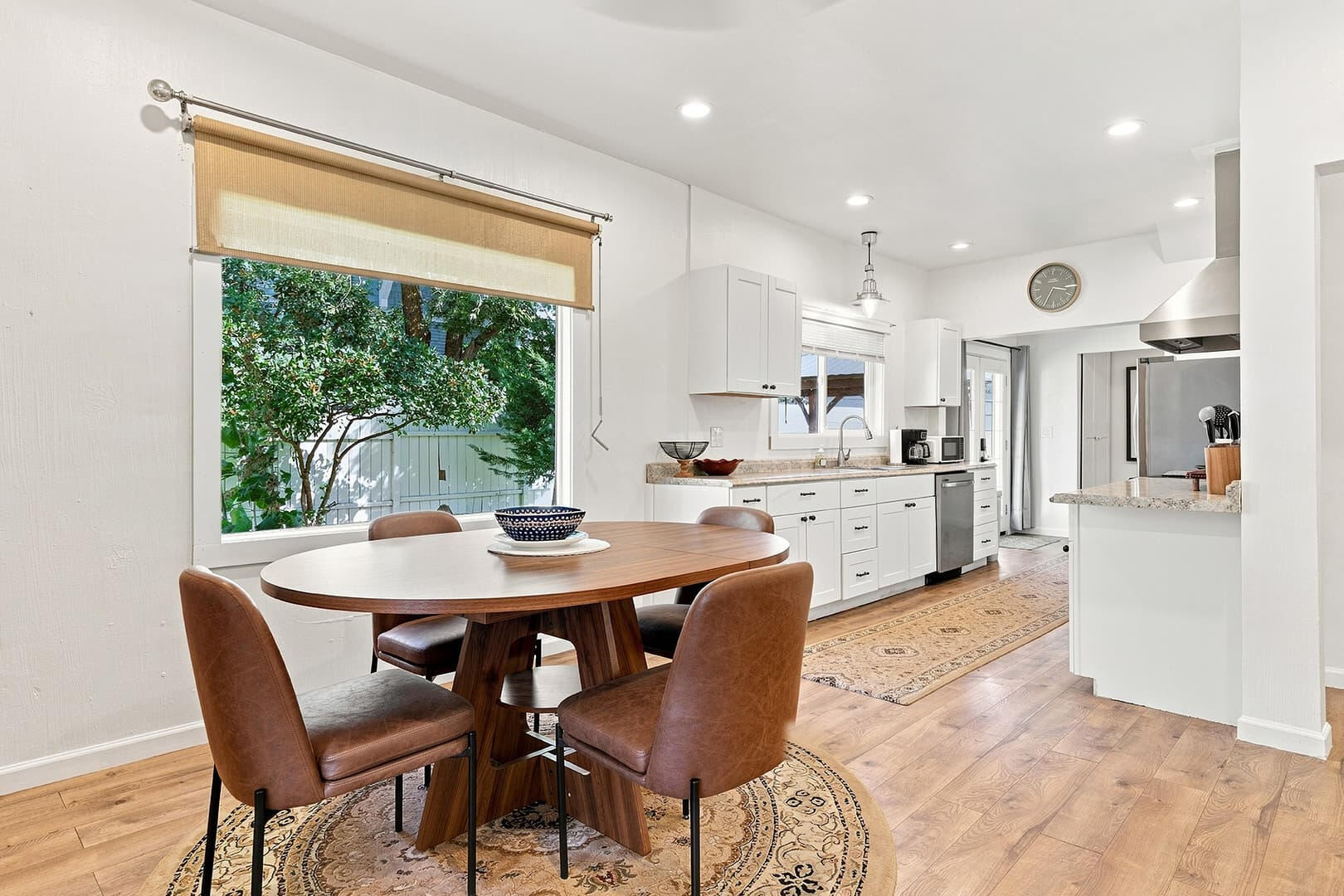 Wooden dining table beside large windows, with the kitchen visible beyond.