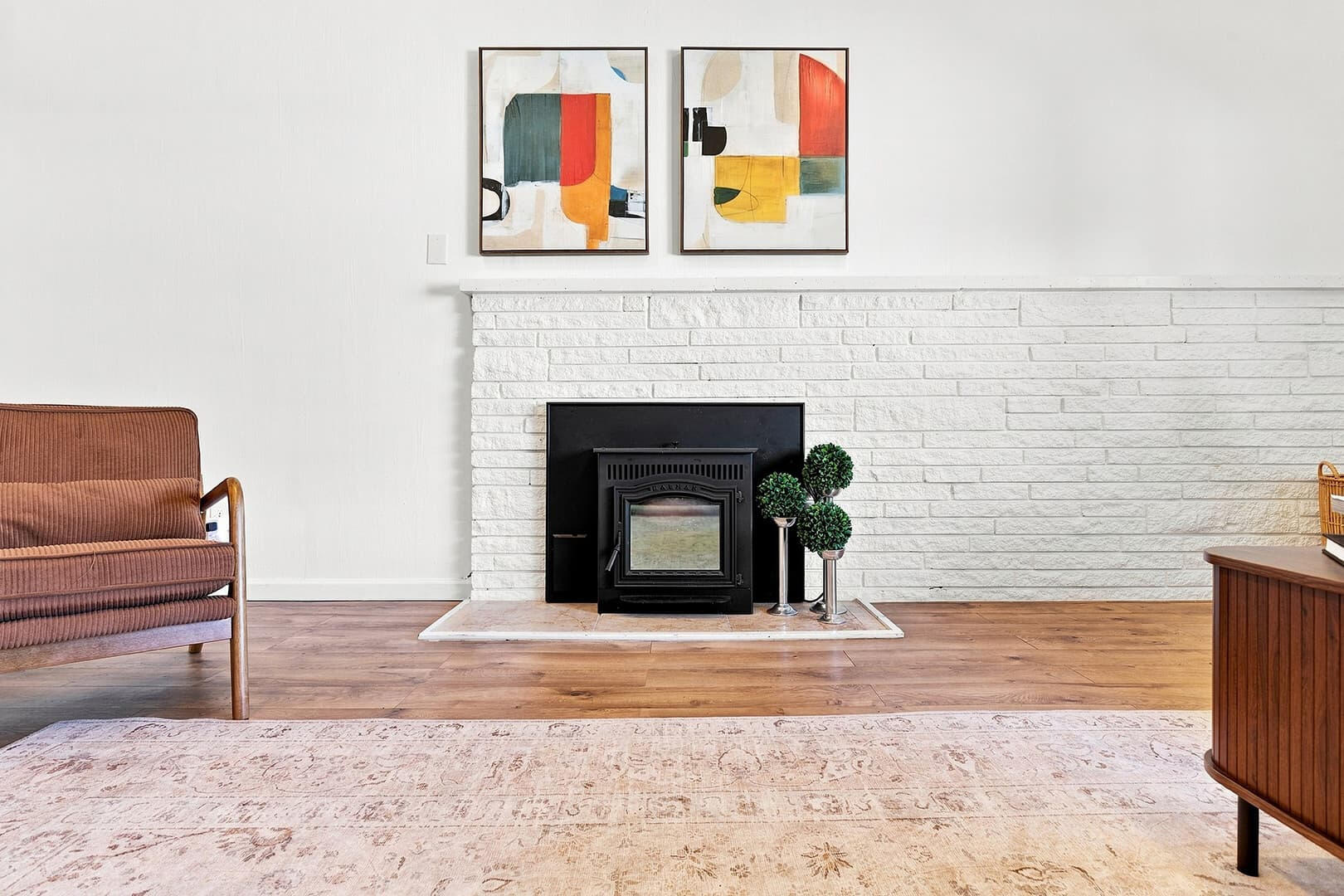 White brick fireplace with a black insert, framed artwork above and a chair to the side.