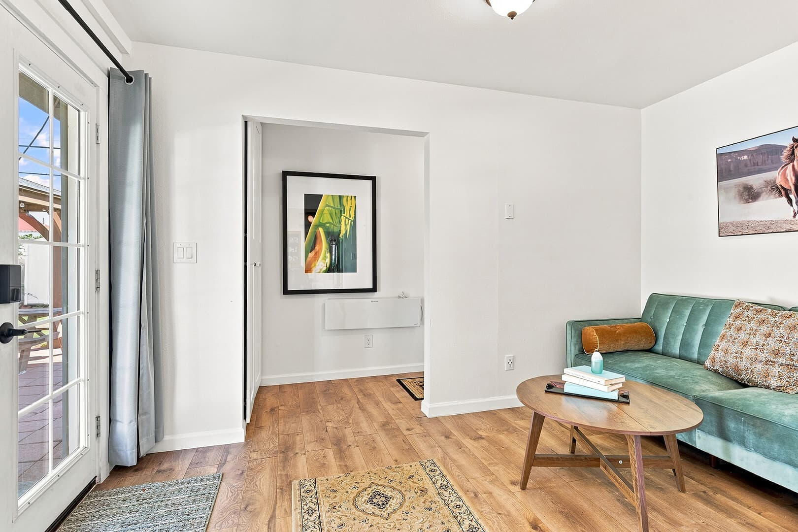 Teal loveseat and wooden coffee table beside a glass door, with wood flooring and framed artwork.