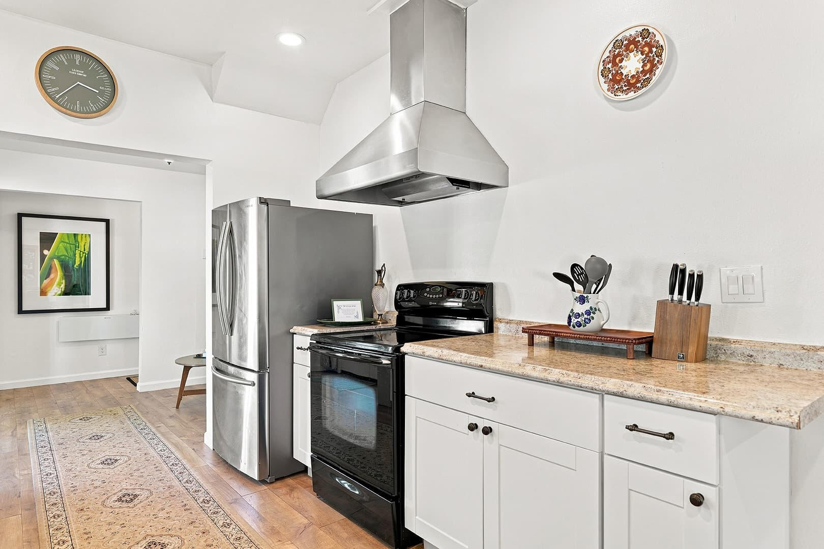 Stove beneath a stainless steel range hood, with a refrigerator and white kitchen cabinets alongside.