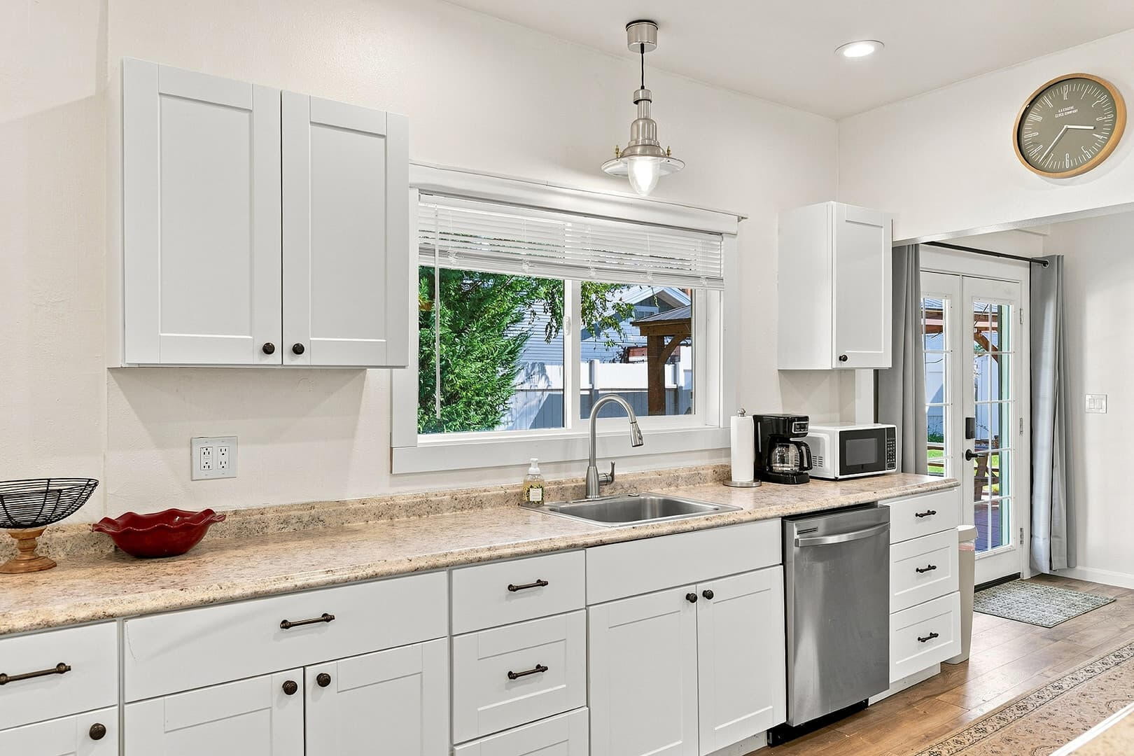Kitchen sink beneath a window, with white cabinets, drawers and countertop space on either side.