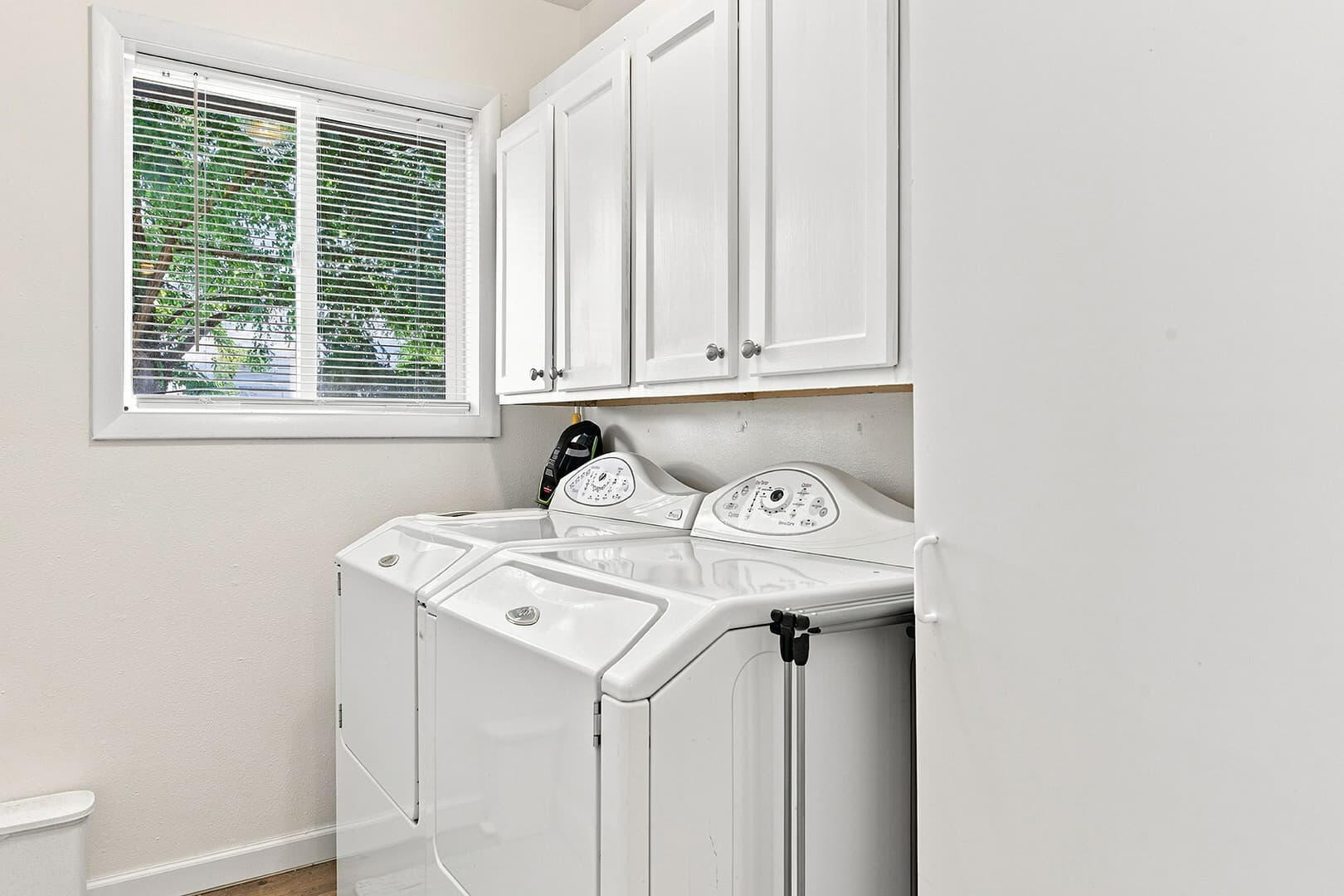 Laundry area with a washer and dryer beneath white wall cabinets, beside a window.
