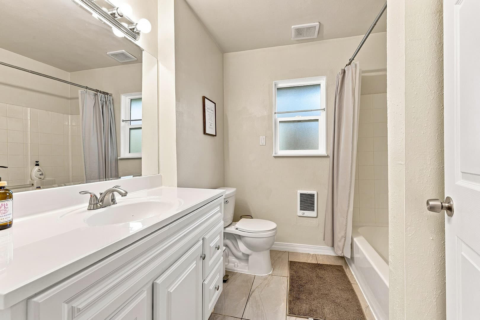 Bathroom with a long vanity, large mirror, toilet and bathtub at Sun Lake Retreat.