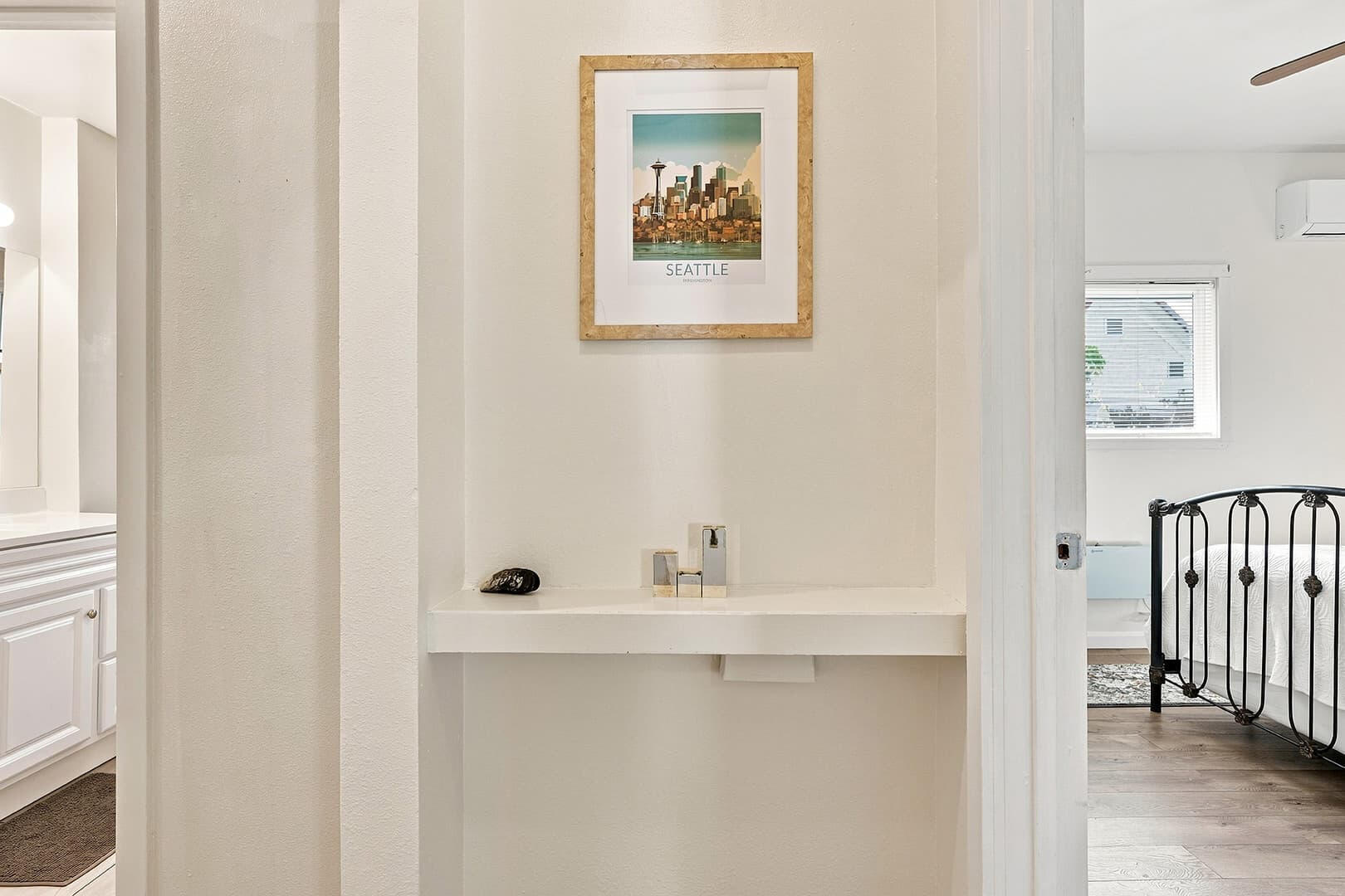 Interior hallway with framed artwork and open doorways toward a bathroom and bedroom.